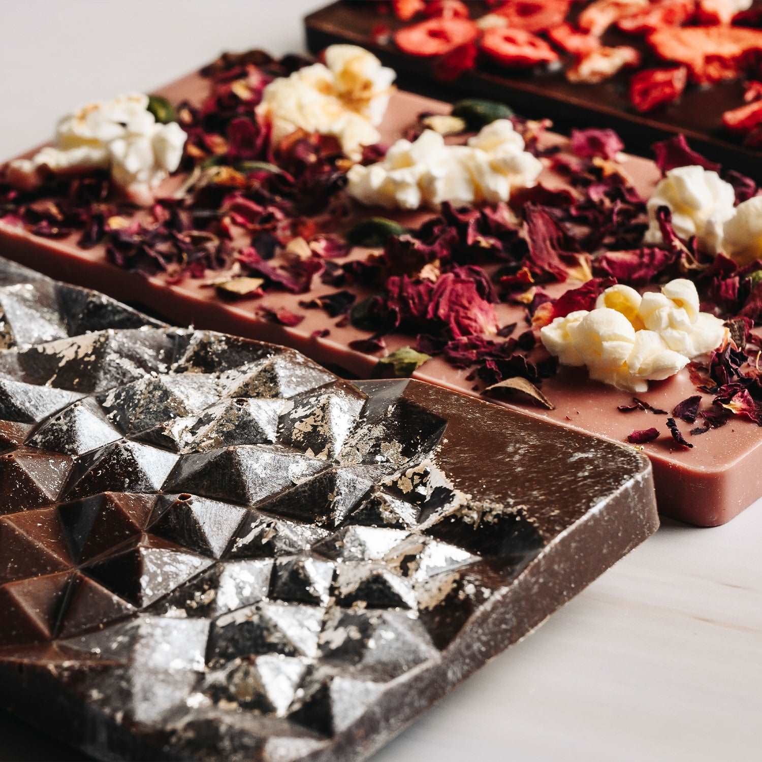 three chocolate bars with silver leaf, milk chocolate, ruby chocolate, dark chocolate. close up of chocolate on white background.